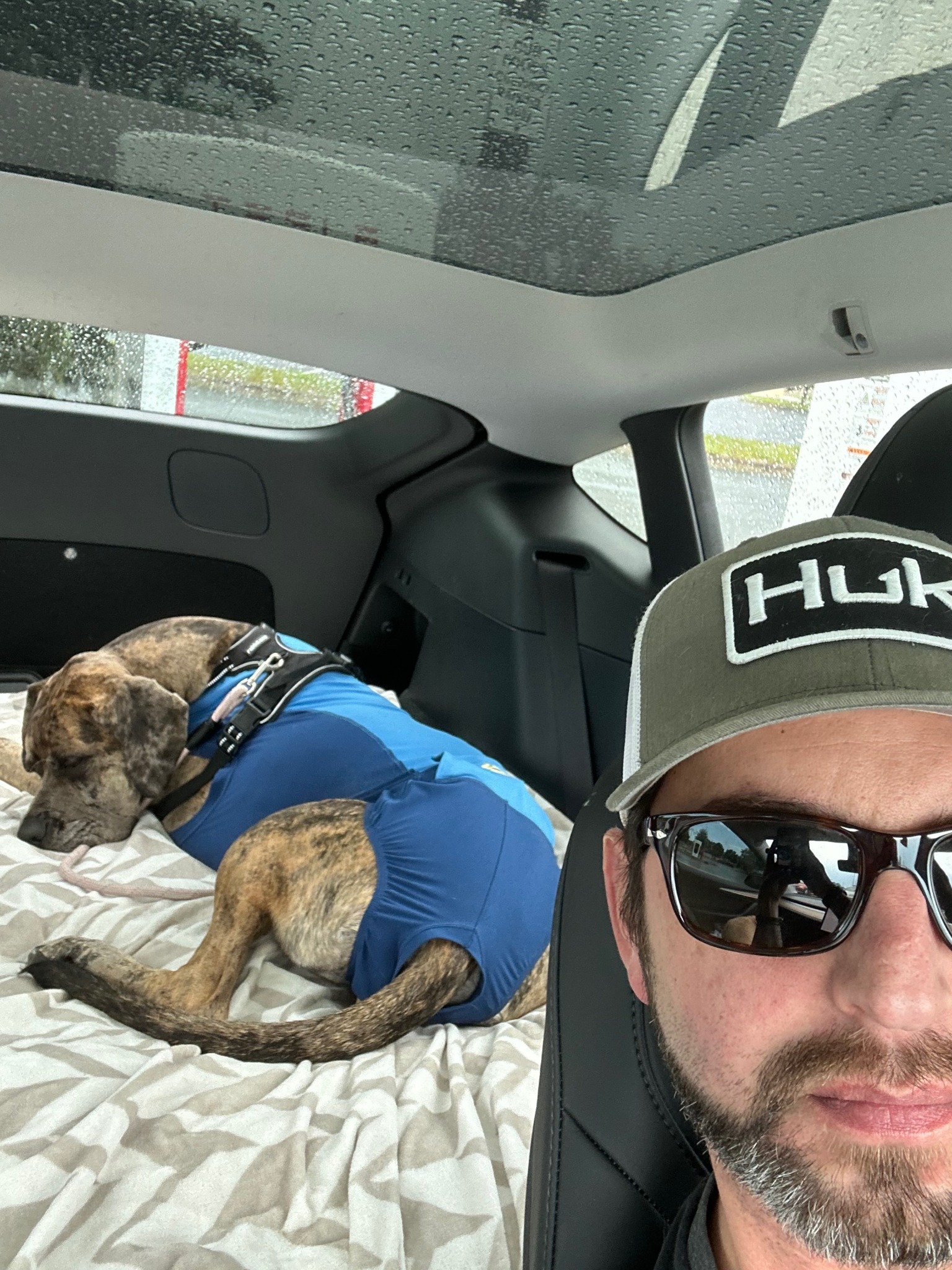 Adam in the car with his dog resting behind him